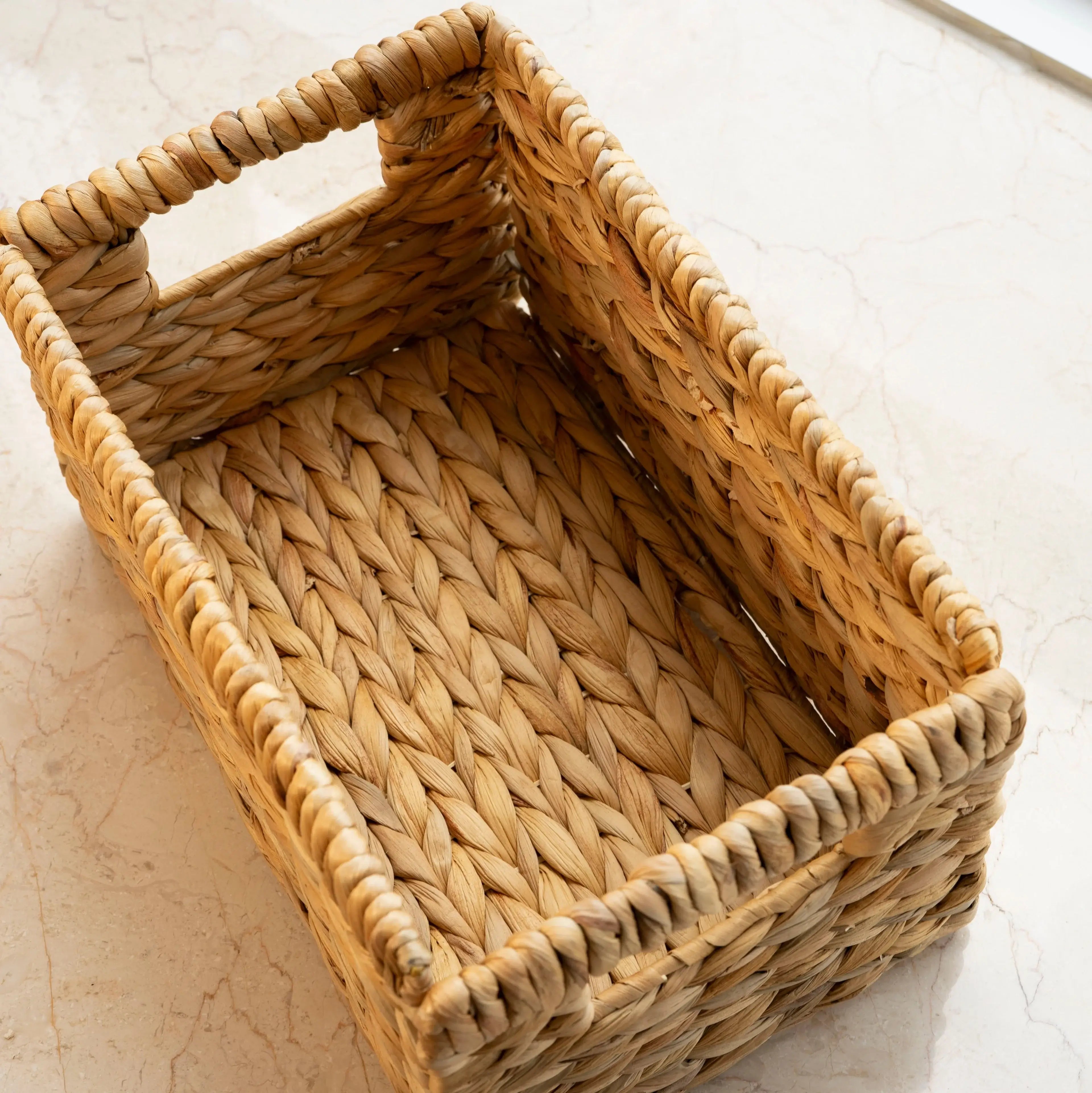 Rectangular woven wicker basket with built-in side handles, placed on a marble surface, showcasing its natural texture and spacious interior for versatile storage and organization