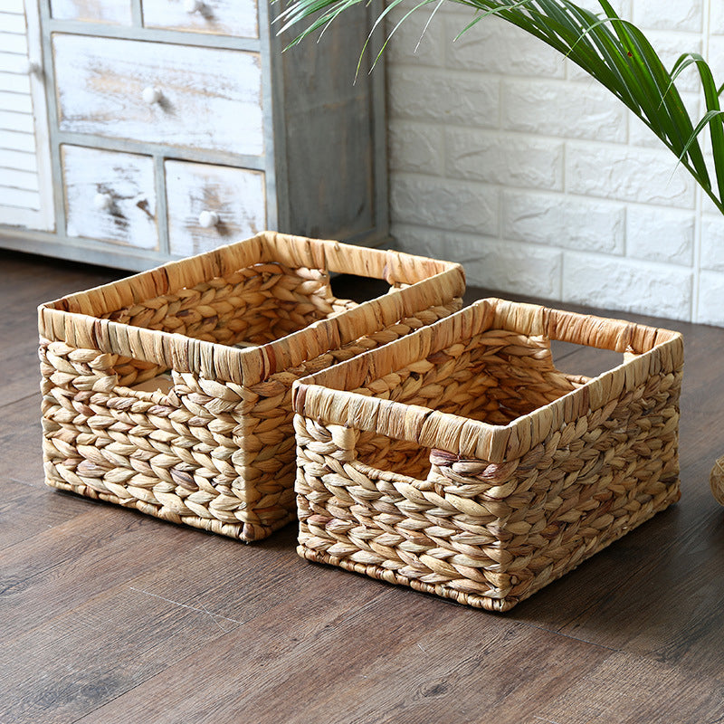 Two rectangular woven wicker baskets with handles placed on a wooden floor in a rustic setting