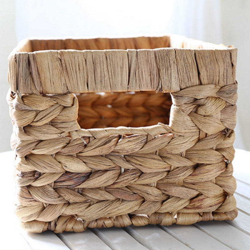 Square woven wicker basket with a built-in handle, placed on a white surface, ideal for storage and organization.