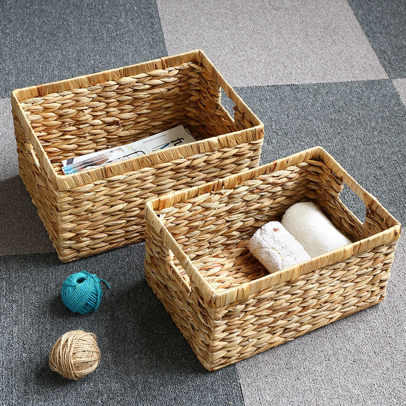 Two rectangular woven wicker baskets on a carpeted floor, one holding towels and the other holding magazines, surrounded by balls of yarn.