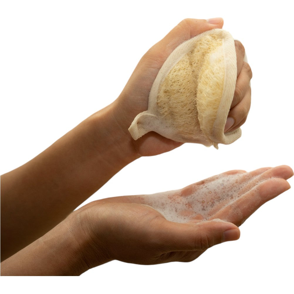 A person using a natural loofah sponge to create foam, holding it in one hand while applying the lather to the other hand, demonstrating the sponge's effectiveness for gentle exfoliation and cleansing.