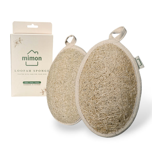 Two oval-shaped natural loofah sponges with fabric edges and hanging loops, accompanied by eco-friendly packaging labeled 'Mimon Loofah Sponge.' Designed for gentle exfoliation and sustainable skincare, handcrafted in Vietnam.